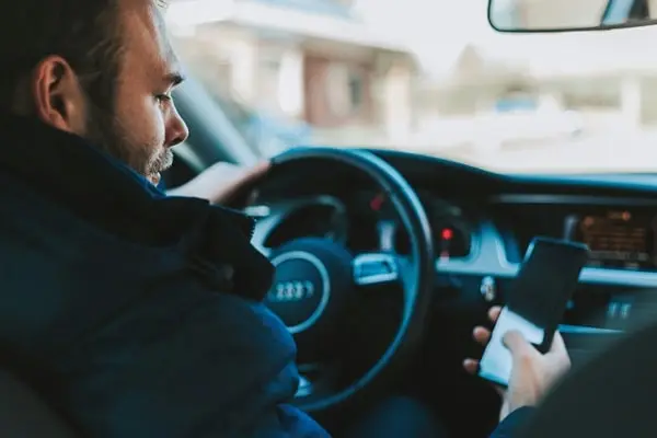 Mann fährt ein Auto und benutzt sein Smartphone.